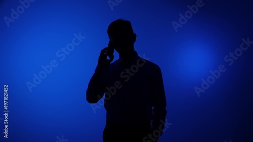 Man silhouette talking on smartphone, communicating and connecting anonymously on a dark blue background, representing concepts of shadow, mystery, and digital interaction