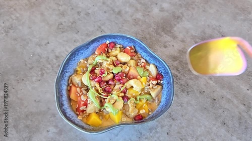Oatmeal cereal porridge with fresh fruits and nuts in blue bowl. Hand scoops up spoonful of porridge Healthy breakfast. Top view on grey stone table.