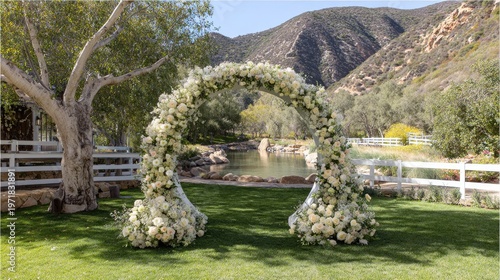 Lavish floral archway stands ready for an outdoor celebration against a backdrop of rolling hills and serene water