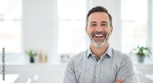 Laughing middle aged businessman wearing patterned shirt standing in bright modern office with blurred white background and house plants indoor