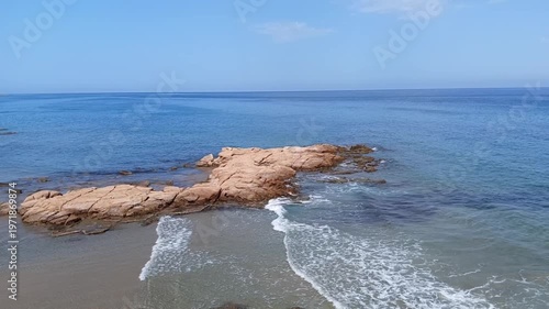 A serene video of a rocky shoreline with waves gently lapping against the shore on a sunny day
