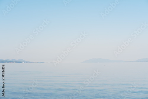 朝霧に包まれた静寂の湖畔、遠くの山並みに灯る光