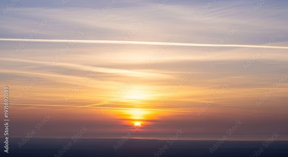 Fototapeta premium A breathtaking sunset with a vibrant orange sky and a setting sun, casting a warm glow over the horizon. The clouds are a mix of warm hues, creating a stunning visual display.