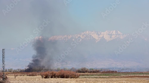 Smoke rising from controlled burn in Utah Valley during the dry spring looking towards Timpanogos Mountain with very little snow from a mild winter.