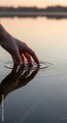 Hand touching calm water surface at sunset.