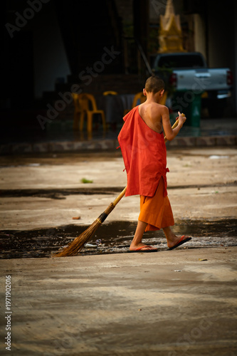 Young monk sweeping in front of temple in Laos