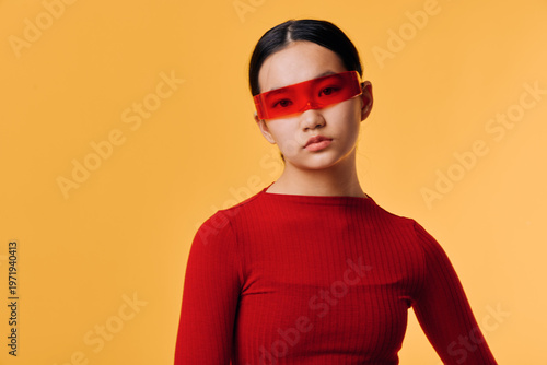 Tableau sur toile Young woman with red sunglasses and red sweater posing in studio with orange background