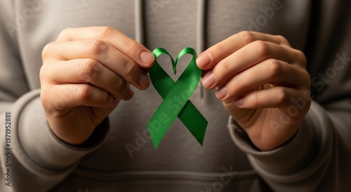 Person holding green awareness ribbon symbol.