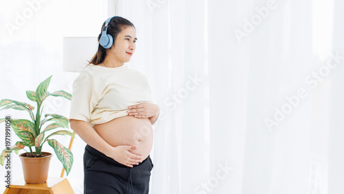 Free Download Asian young pregnant woman standing near window in living room relaxing listening to music touching belly care peaceful comfortable love healthy happy pregnancy motherhood maternity tummy wellness. - GFXLoad