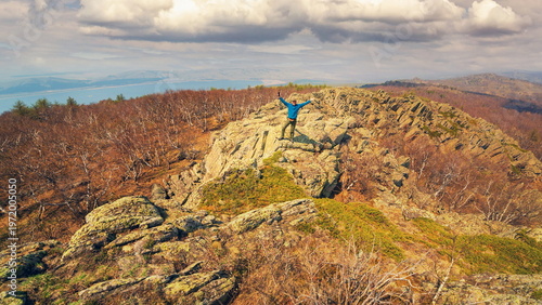 an elderly happy tourist stands on a high rock against the backdrop of the Ural mountains on a summer day