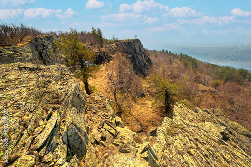 an elderly happy tourist stands on a high rock against the backdrop of the Ural mountains on a summer day