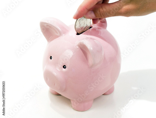 hand putting a coin into a pink piggy bank