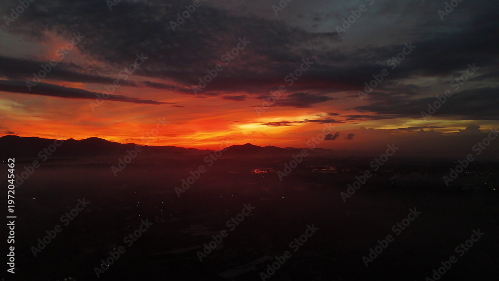 Obraz premium Breathtaking Sunset Over Mountain Range with Fiery Sky and Hazy Valley Landscape