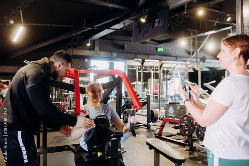 Fotografie In a lively gym setting, a trainer assists a woman in her workout, offering support and motivation
