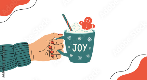 Hand holding a blue mug of steaming hot cocoa topped with whipped cream and a gingerbread man cookie with the word joy written on the cup.