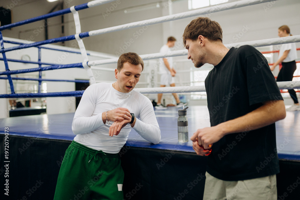Fototapeta premium Boxers discuss training techniques and strategies while checking the time during a busy practice session. The mood is friendly yet competitive, showcasing dedication to the sport.