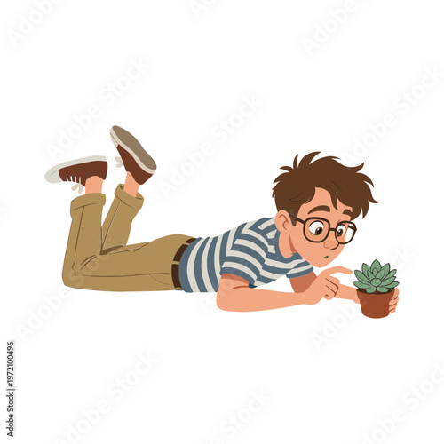A boy lies on his stomach holding a potted succulent plant closely.