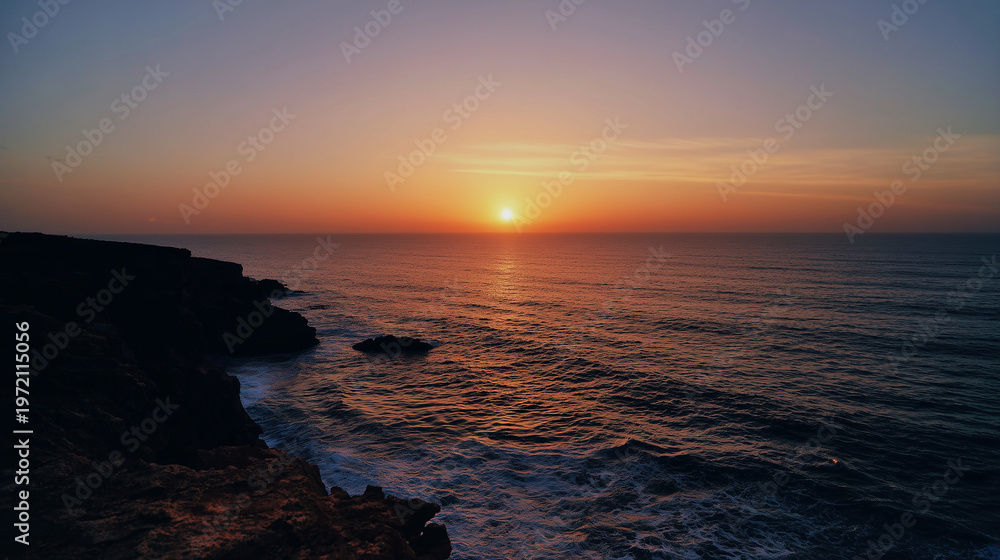 Obraz premium The edge of a cliff at sunset with the sun dipping below the horizon of the sea