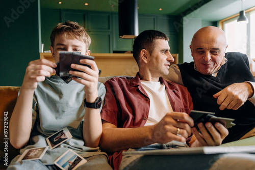 Obraz na plátne A young boy and two adult men sit together on a sofa in a room with green walls