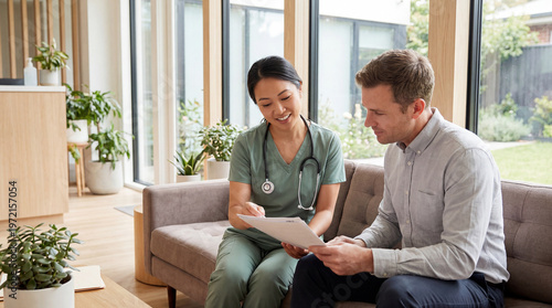 Smiling female doctor in scrubs provides a personalized medical consultation, explaining documents to a male patient in a modern clinic