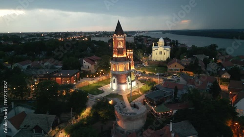Dramatic aerial rotation of illuminated Gardos tower at night under a stormy sky with background lightning, Zemun, Belgrade, Serbia.