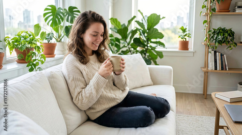 Young woman enjoying coffee break while working on laptop in bright home office with plants
