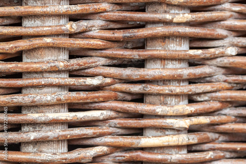 Macro shot of a traditional wicker fence made of intertwined brown wooden branches. Rustic natural texture and rural craft pattern.