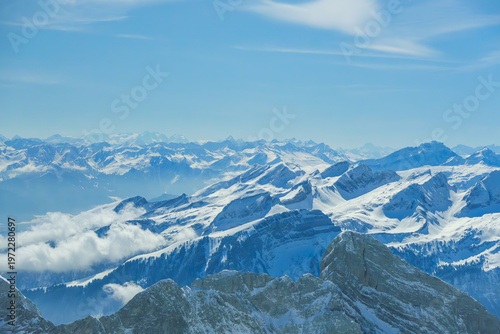 Snow covered mountain range under clear blue sky, showcasing majestic peaks and ridges. serene landscape is enhanced by scattered clouds, creating breathtaking view of nature beauty
