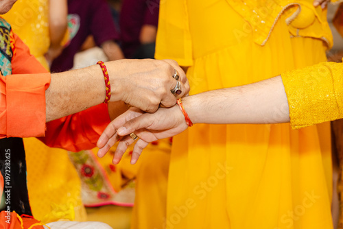 Quadro em tela A woman in a yellow dress is having a red thread tied around her wrist by anothe