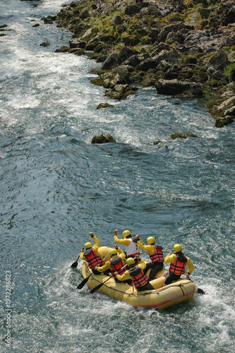 Obraz na płótnie A group of rafters in a yellow boat wearing helmets and life jackets paddling th
