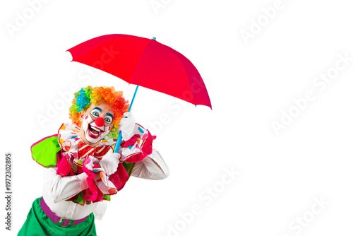 Funny clown holding orange umbrella. Entertainer Joker in colorful suit and wig. Buffoon with clown whiteface makeup. Professional actor at event, kid's party, circus