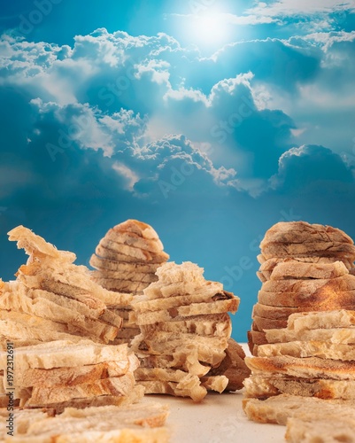 Bild auf Leinwand In a dreamlike landscape, towering formations of bread rise like mountains beneath a vibrant blue sky sprinkled with fluffy clouds