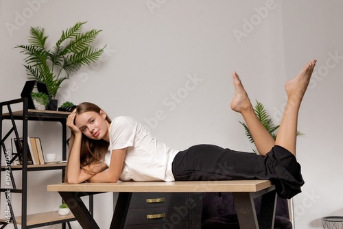 Woman relaxes on desk with legs up in modern indoor space with plants