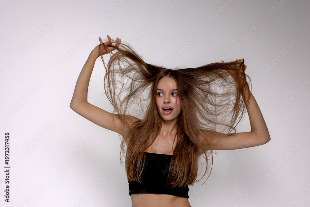 Fototapeta premium Young woman playfully poses with long hair on a plain background during a studio photoshoot session