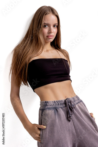 Young woman posing in casual outfit with black crop top and gray pants against a white background