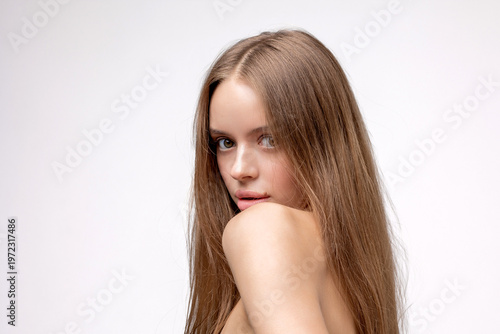 Young woman with long hair looking back over her shoulder in a studio setting with plain background