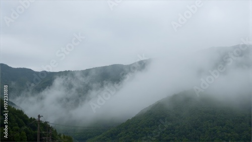 Landscape of mist-covered mountains with greenery at the base.