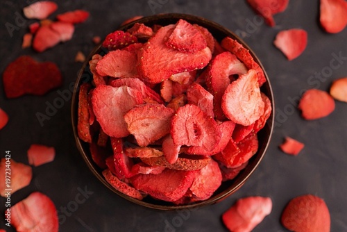 Top view of freeze-dried strawberry slices in a wooden bowl on dark background