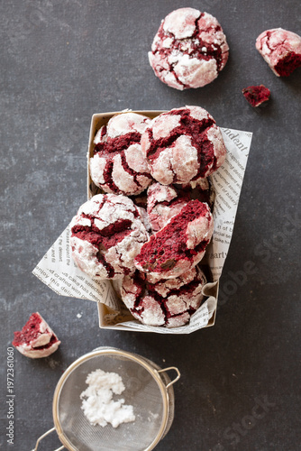 Red velvet cookies in a decorative box with powdered sugar on a dark textured surface