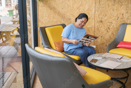 Woman reads menu while sitting in a cafe with comfortable chairs and wooden decor during afternoon hours