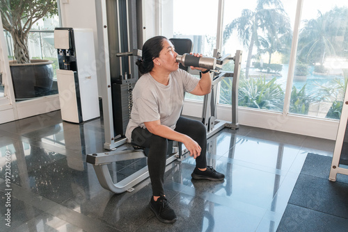 Woman exercises in gym and takes a break with a drink in hand during morning workout session near window