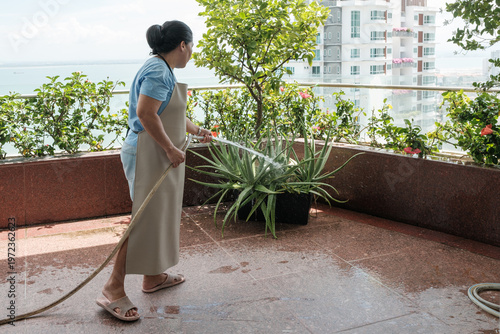 Woman waters plants on a balcony with a hose in a city setting by the water during daytime
