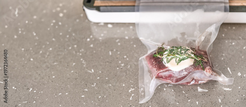 Single raw beef steak with rosemary and butter in vacuum bag near sealer wide shot sous vide