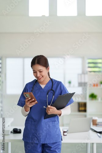 Asian adult healthcare professional woman smiling happy using smartphone clipboard modern clinic hospital office