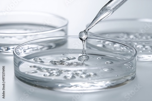 Close-up of a pipette dripping clear liquid into a petri dish in a laboratory setting.