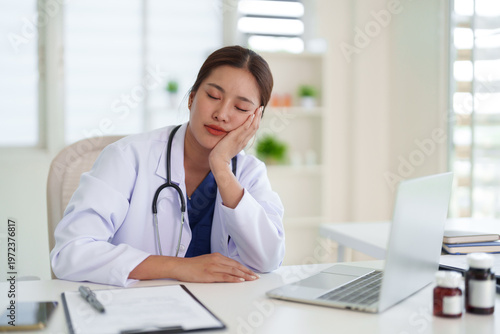 Asian adult female doctor feeling exhausted resting head on hand sleeping desk office after long shift working healthcare professional burnout fatigue stress concept