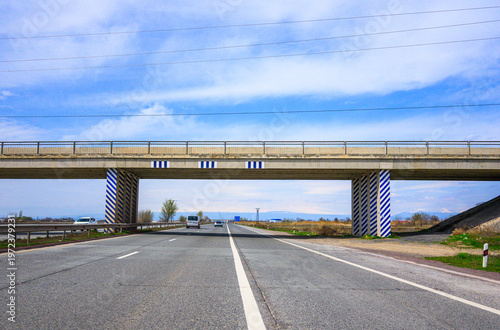 Long straight road under modern bridge with striped pillars