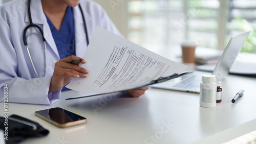 Obraz na plátně Asian adult woman doctor reviewing patient medical form paperwork laptop desk cl