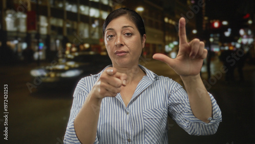Tableau sur toile Hispanic woman making loser gesture with one hand and pointing finger toward camera on street; mockery