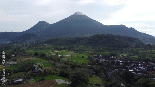 Aerial view of Mount Penanggungan with lush rice fields, village landscape, and camping area under a calm sky, showcasing natural beauty and rural life in East Java